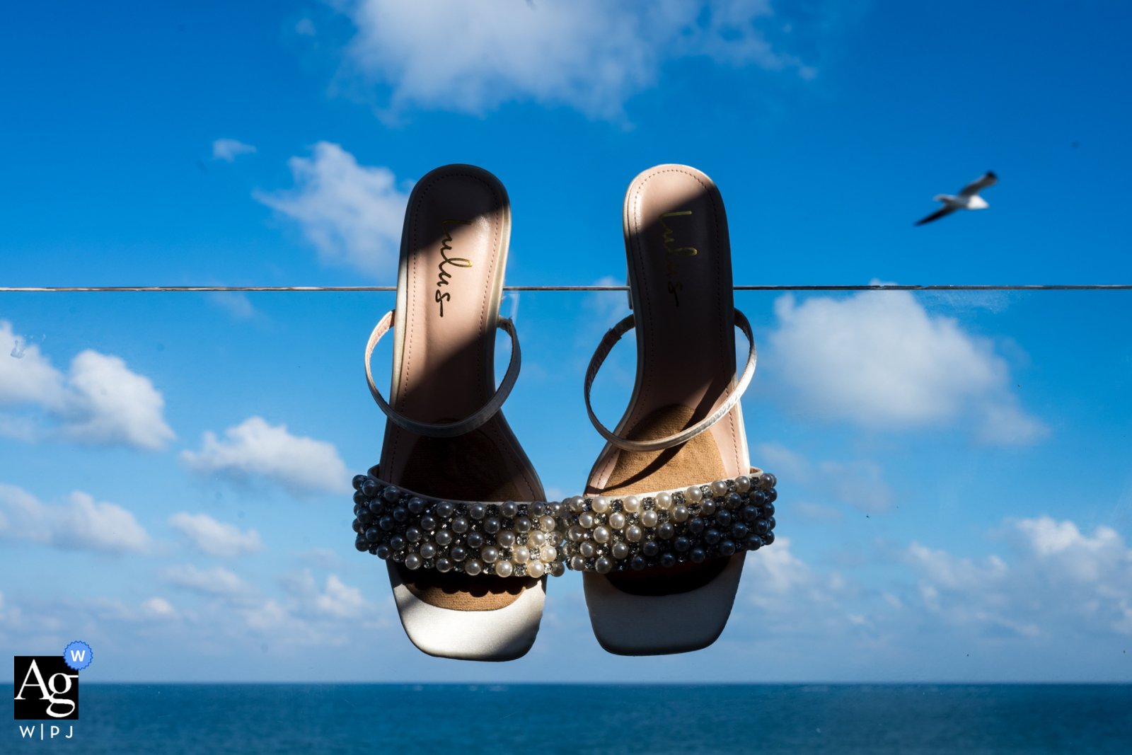 Sandales de la mariée suspendues à un fil face à la mer — photo récompensée Artistic Guild V02 2026